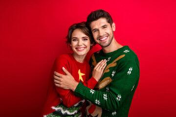 Photo of funky dreamy married couple wear ornament sweaters embracing isolated red color background
