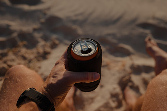 Man holding a can of drink at sunset on the beach, point of view angle (POV).