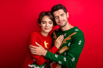 Photo of dreamy sleepy married couple wear ornament sweaters embracing closed eyes isolated red color background