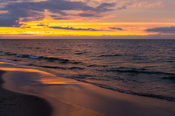 Fototapeta premium Orange sunset over the sea. Waves crashing onto the beach, dramatic sky. A static shot taken in the early evening