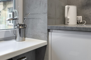 A white windowsill in the kitchen, with cooking utensils and a white kettle on it