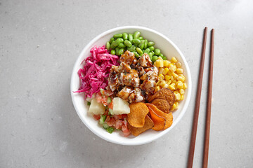 top shot of a bowl of chicken vegetable salad with wooden chopsticks on top of a grey background