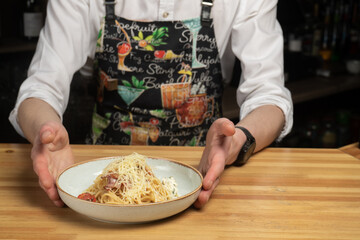 A plate of pasta stands on a wooden table with male hands