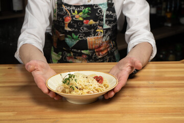 A plate of pasta stands on a wooden table with male hands