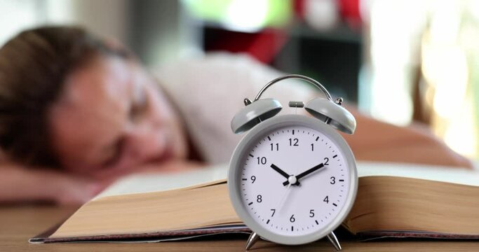 Alarm clock on open book woman lies and sleeps on table. Overstudy and insomnia and overwork