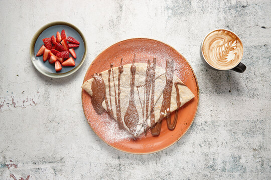 Top view down of crepe with chocolate sauce  with strawberries and cup of coffee on the side