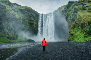 Powerful Skogafoss waterfall and male tourist walking in summer at Iceland - obrazy, fototapety, plakaty