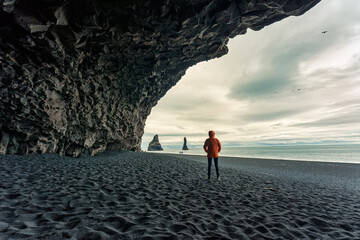 Reynisdrangar natural rock formation with female tourist standing in halsanefshellir cave on black sand beach in summer at Iceland - obrazy, fototapety, plakaty