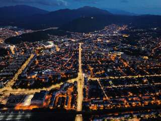 Beneath the night sky, an aerial panorama of Brașov city in Romania is unveiled as a luminous pattern of interconnected streets.