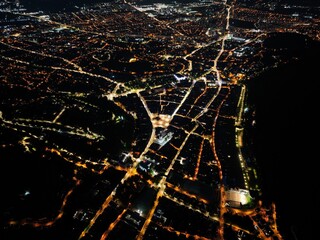 An aerial night panorama of Brașov city in Romania. Street lamps illuminate the city's arteries, casting a golden glow upon the urban landscape.