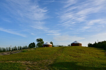 Obraz premium A close up on two temporary houses or huts similars to the ones used and built by nomadic tribes located on the top of a hill, next to a wooden fence, spotted on a cloudy summer day in Poland