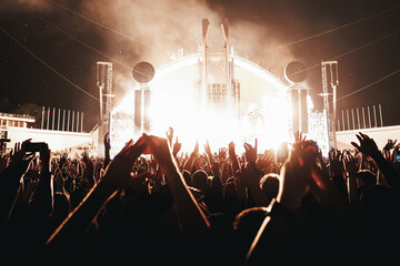 Performance of a popular group. The crowd with raised hands against the stage light