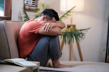 Unpleasant pain. Sad unhappy handsome man sitting on the sofa and holding his forehead while having headache