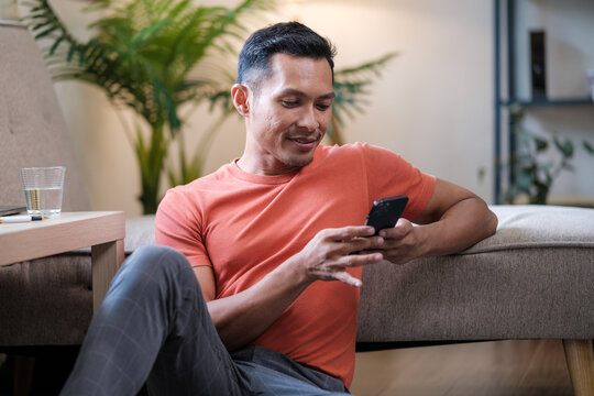 Happy, man and texting on cellphone in living room for online mobile app, scroll social media and notification on sofa. Asian male person typing on smartphone, contact and internet download at home