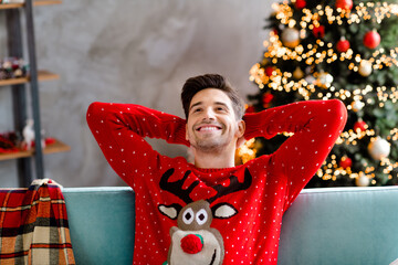 Photo portrait of funky young male wear red christmas sweater happy holidays beautiful living room decorated theme party hands behind head
