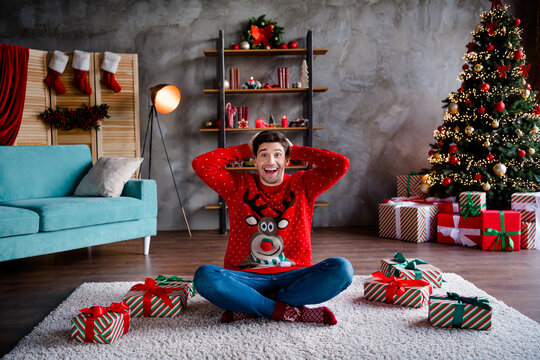 Full size photo of astonished nice young man sit carpet floor hands touch head multiple christmas morning giftbox living room indoors