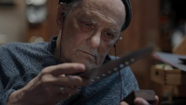 Senior gray haired male master in a wheelchair working at his workshop sharpening Japanese kitchen knife