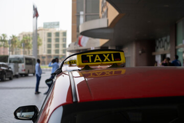 Sign taxi on the car roof that is parked next to hotel entrance. Selective focus, blurred background.