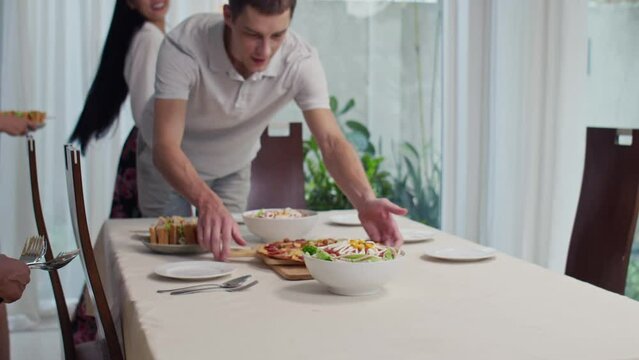 Cropped shot of multicultural friends preparing table for festive dinner with dishes and wine