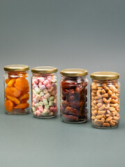 Group of jars with cashew nuts, dried apricots, dates and marshmallow on  plain background