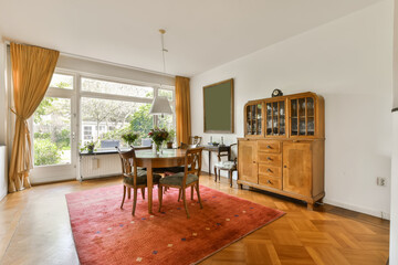 a dining room with wood flooring and wooden furniture in the center of the room there is a large window that looks out onto the yard