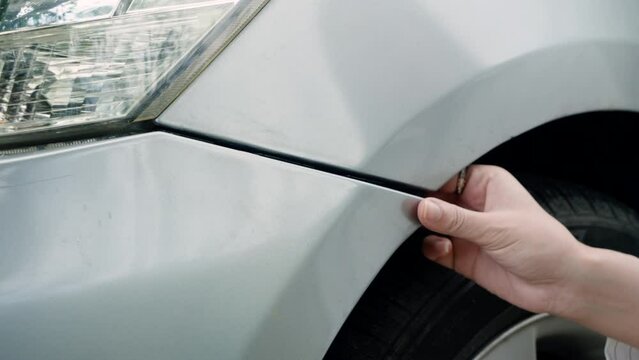 Close-up of a car bumper that caused damage from the collision There are women's hands holding and inspecting damage. Before calling an insurance official to claim insurance, send the car for repairs