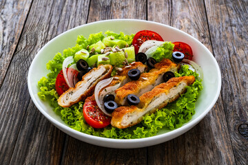 Caesar style salad - fried breaded chicken breast and vegetables on wooden table
