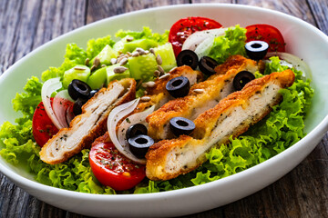 Caesar style salad - fried breaded chicken breast and vegetables on wooden table
