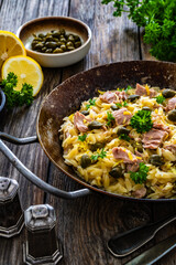 Mediterranean orzo salad with tuna, lemon and capers on wooden background
