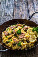 Mediterranean orzo salad with tuna, lemon and capers on wooden background