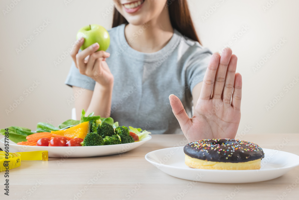 Sticker Woman on dieting for good health concept. Close up female using hand push out her favourite donut and choose salad vegetables for good health.