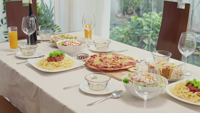 Close up of festive table with pizza, pasta, salad and wine in room in pastel colours with nobody aroundClose up of festive table with pizza, pasta, salad and wine in room in pastel colours with nobod