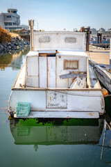 The back of an old wooden sea vessel in white color stands in clear water in the harbor
