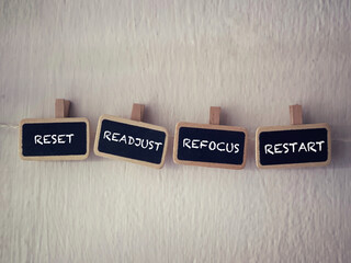 Motivational and inspirational words. RESET, READJUST, REFOCUS, RESTART written on wooden tags. With blurred styled background.