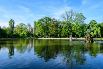 Vivid green landscape with old large linden trees and small boats near the lake in Cismigiu Garden (Gradina Cismigiu), a public park in the city center of Bucharest, Romania, in a sunny spring day.