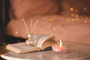 Liquid home fragrance in glass bottle with bamboo sticks and scented candle with open paper book on...