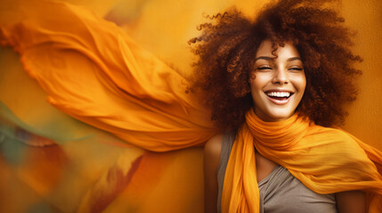 A beautiful, smiling African-American woman with wildly curly afro hair and a long scarf around her neck, billowing in the wind around her in autumn colors.