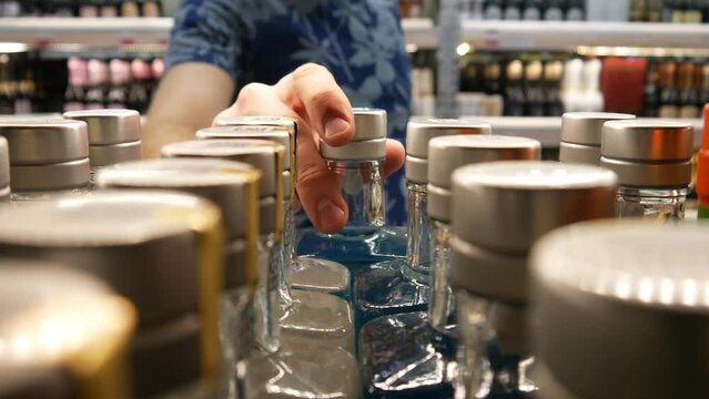 Close-up of many bottles of blue gin in alcohol department and a buyer chooses one