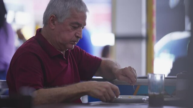 Candid senior man eating lunch in restaurant, casual everyday scene of older person during meal time at diner