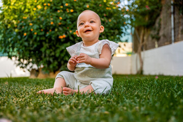 little barefoot baby plays sitting on the floor of the garden at home laughing. concept development and learning in childhood