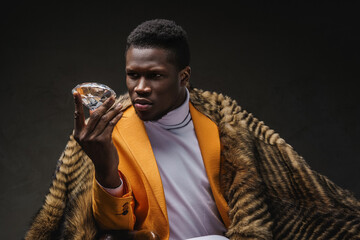 A well-dressed dark-skinned man holding a large diamond while draped in a wild animal skin on a...
