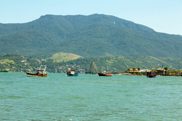 Barcos navegando em mar calmo, céu azul, dia de sol e montanhas ao fundo. São Sebastião, Litoral...