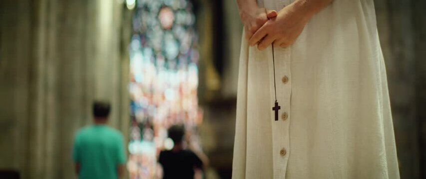 Woman praying in the old church. Adult girl parishioner holding a religious wooden cross in hands.