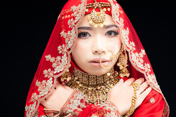 Close up portrait of a beautiful Asian Muslim lady in a hijab wearing a gorgeous Bollywood or Indian themed red traditional wedding dress isolated on dark background