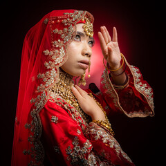 Close up portrait of a beautiful Asian Muslim lady in a hijab wearing a gorgeous Bollywood or Indian themed red traditional wedding dress isolated on dark background