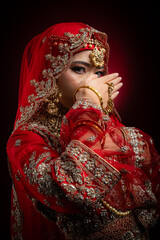 Close up portrait of a beautiful Asian Muslim lady in a hijab wearing a gorgeous Bollywood or Indian themed red traditional wedding dress isolated on dark background