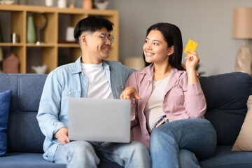 Obraz premium Cheerful Japanese spouses buyers shopping online in living room