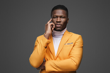 Close-up portrait of a thoughtful dark-skinned man in an elegant yellow jacket and white turtleneck posing on a gray background