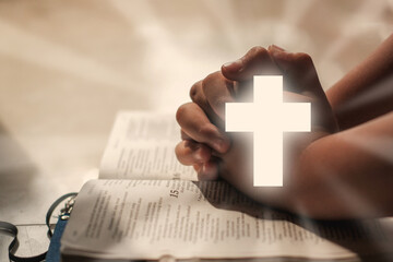 Christian Religion concept background. Hands folded in prayer on a Holy Bible with shining cross