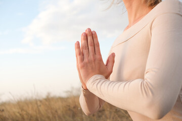 Female hands in prayer pose against nature and blue sky. The concept of harmony and healthy lifestyle.